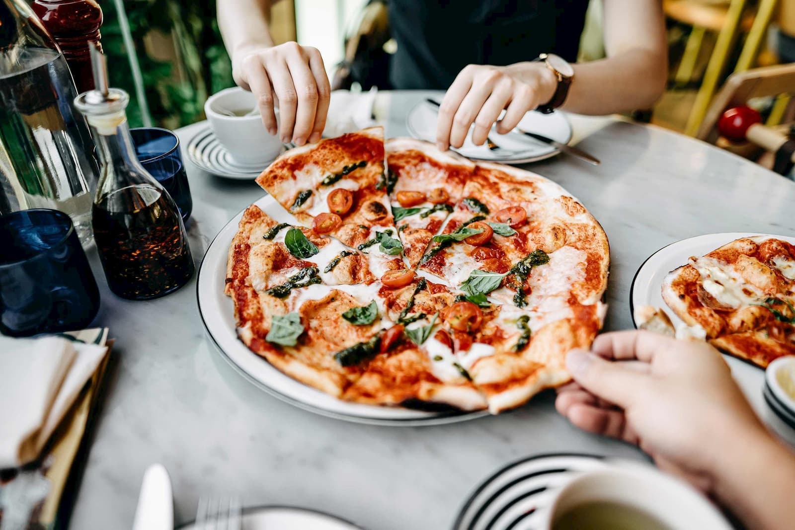 Hands reaching for slices of Margherita pizza topped with basil and cherry tomatoes