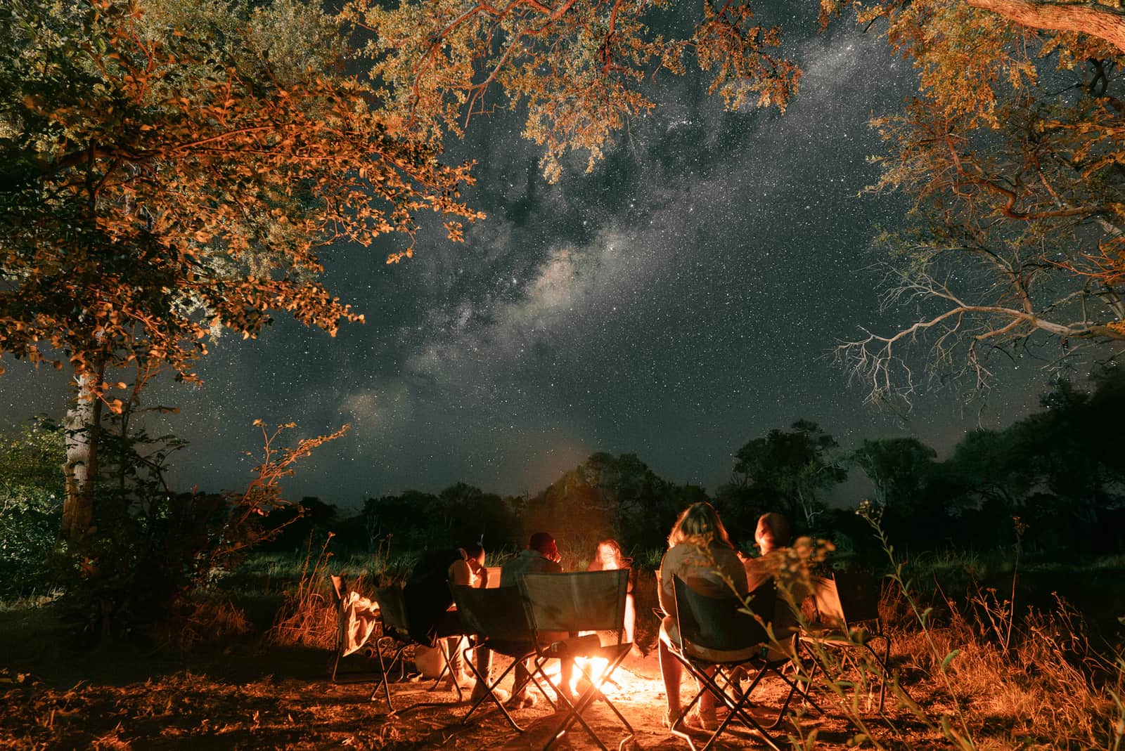 Travellers sat around campfire under a starry sky in the Okavango Delta, Botswana