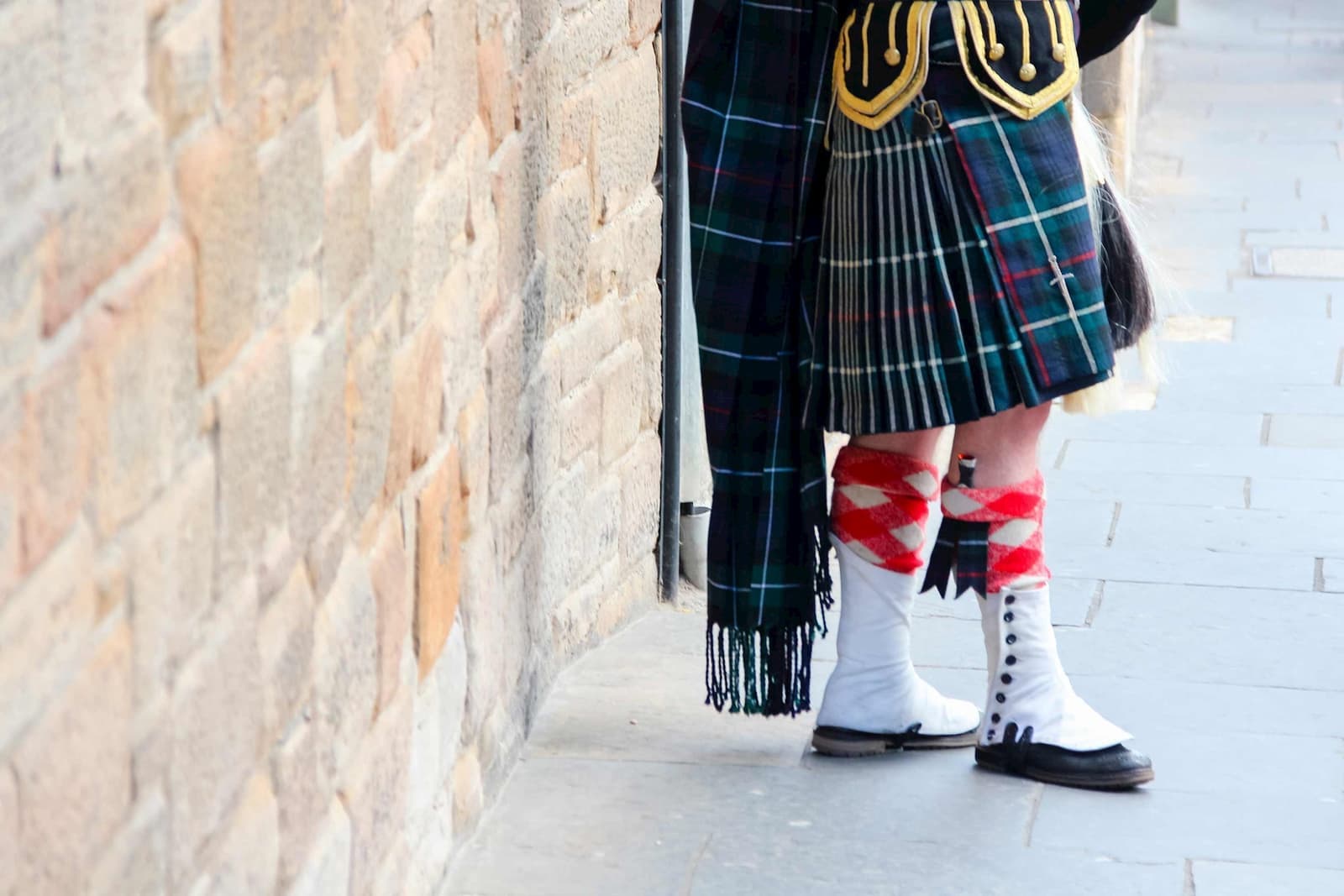 A close-up of a person wearing a Scottish kilt standing against a stone wall