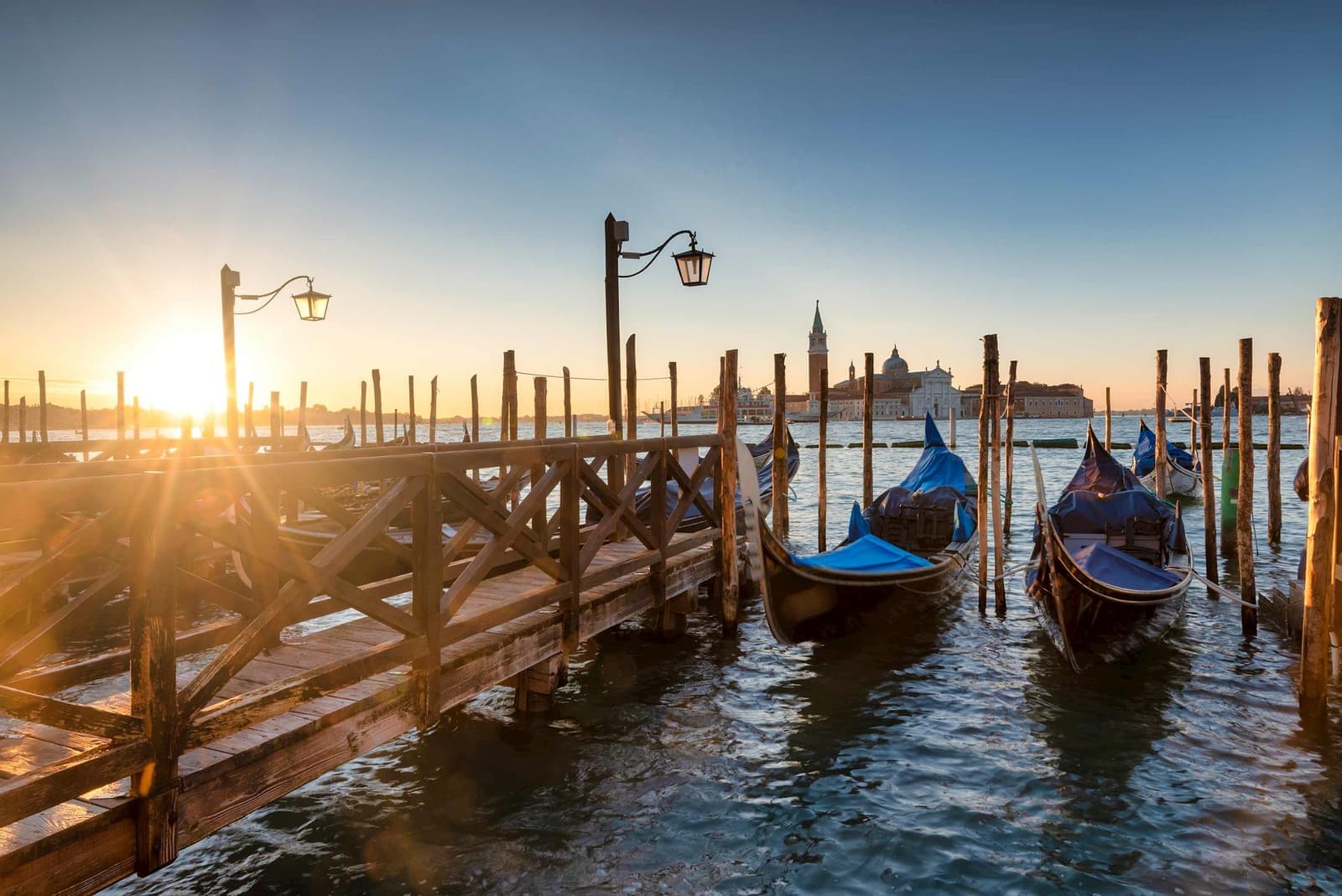 Gondolas moored at wooden dock in Venice with lampposts and San Giorgio Maggiore church at sunrise
