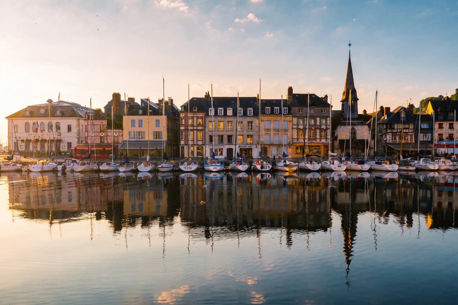 The Vieux Bassin in Honfleur, France, reflecting colorful buildings at sunset.
