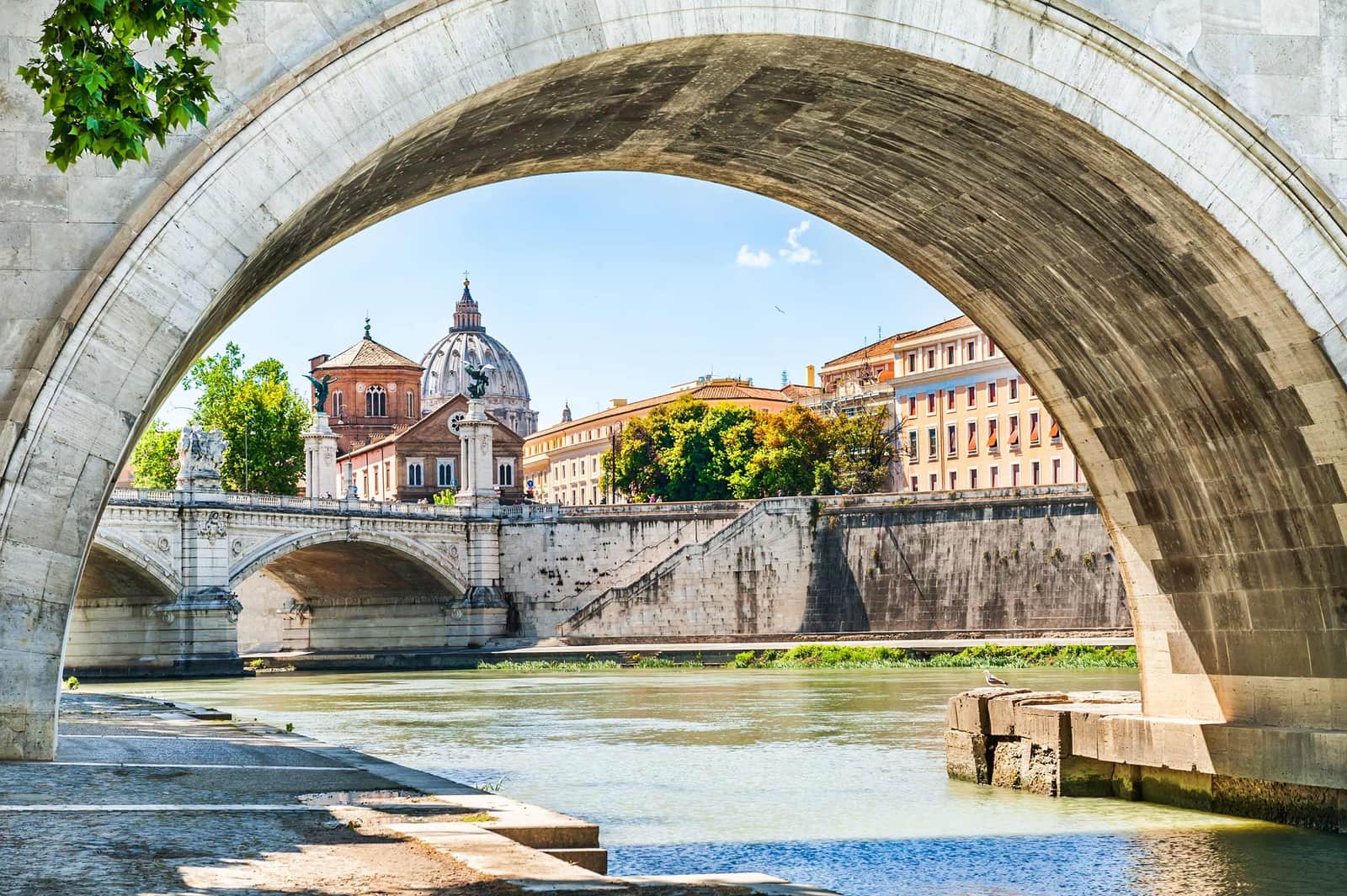 St. Peter’s Basilica dome framed by stone bridge arch over Tiber River in Rome
