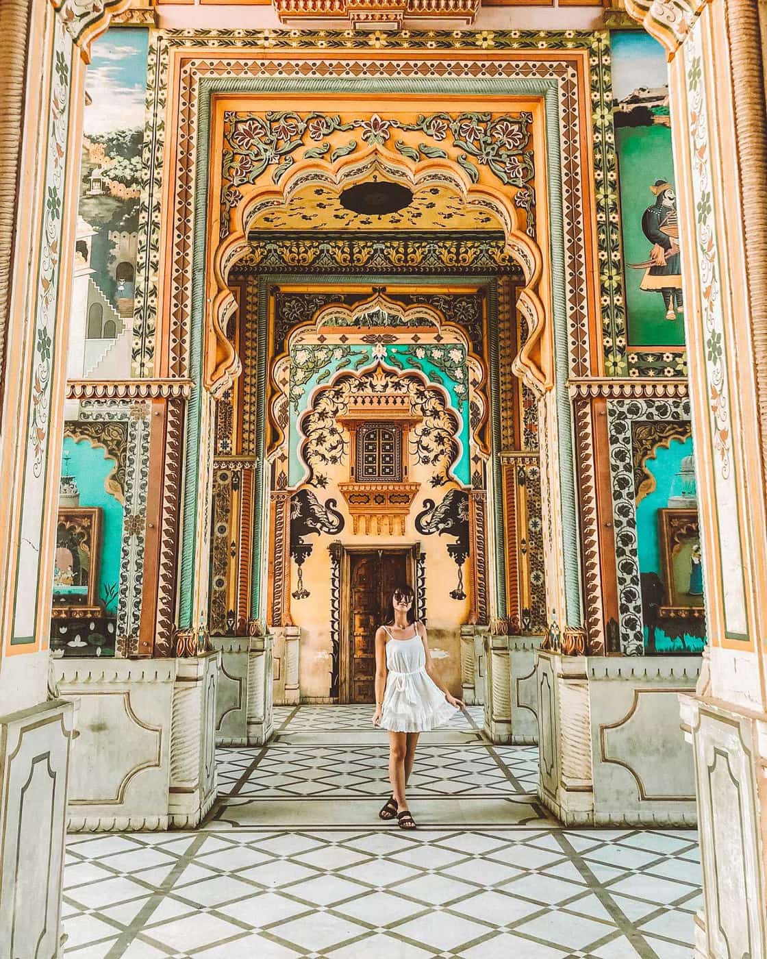 Traveller stands under vibrant, Rajasthani archway filled with intricate murals, Jaipur, India