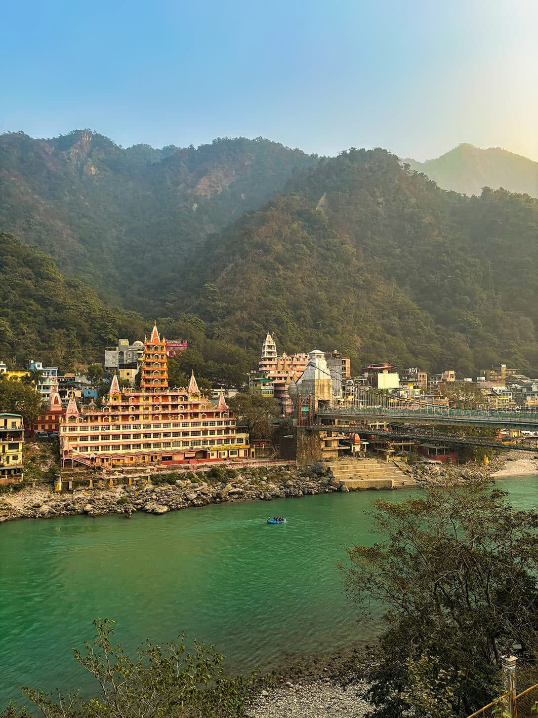 Multi-story orange temple by river with misty mountains, Rishikesh, India
