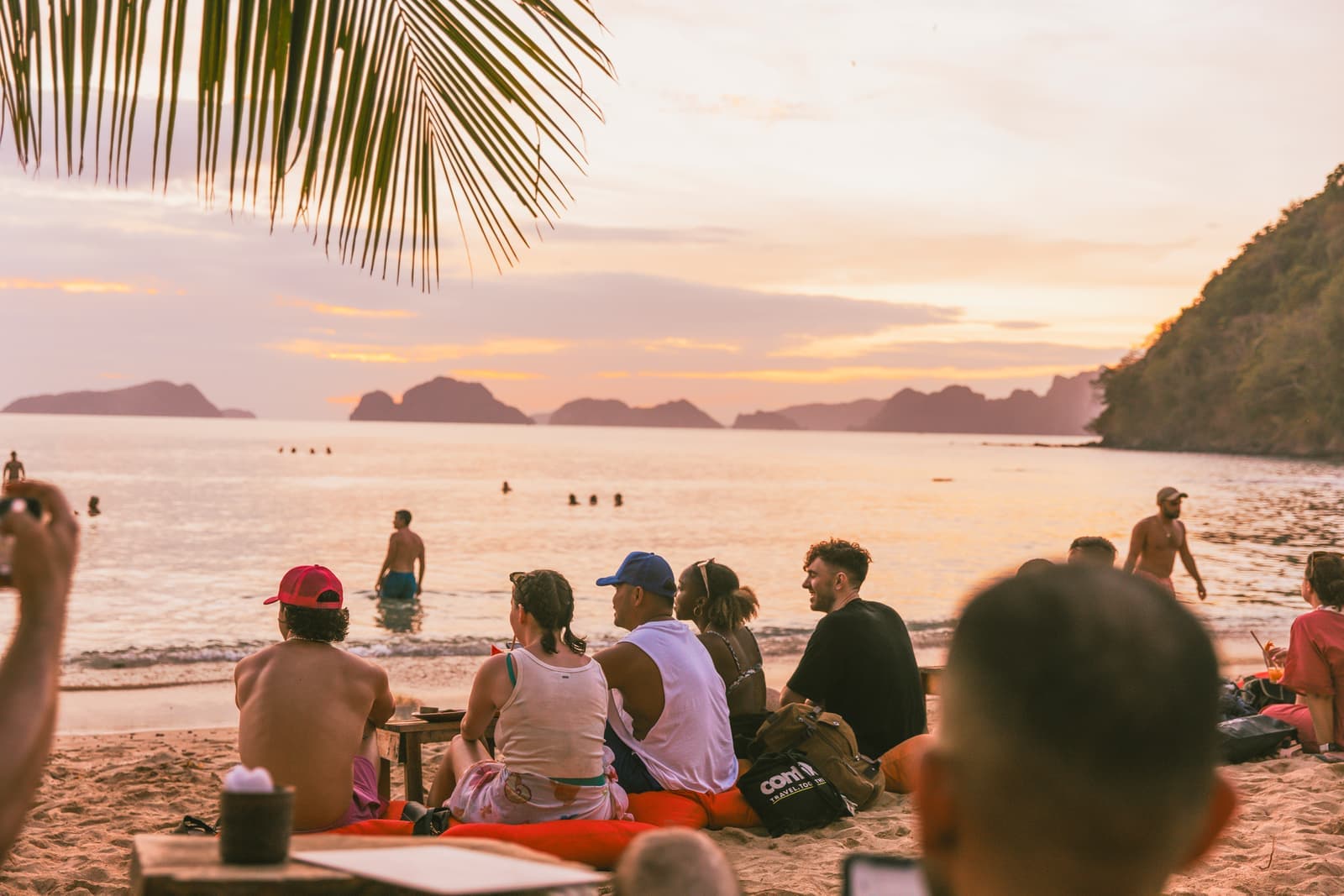 Travellers sitting on the beach looking out at the sunset in the Philippines