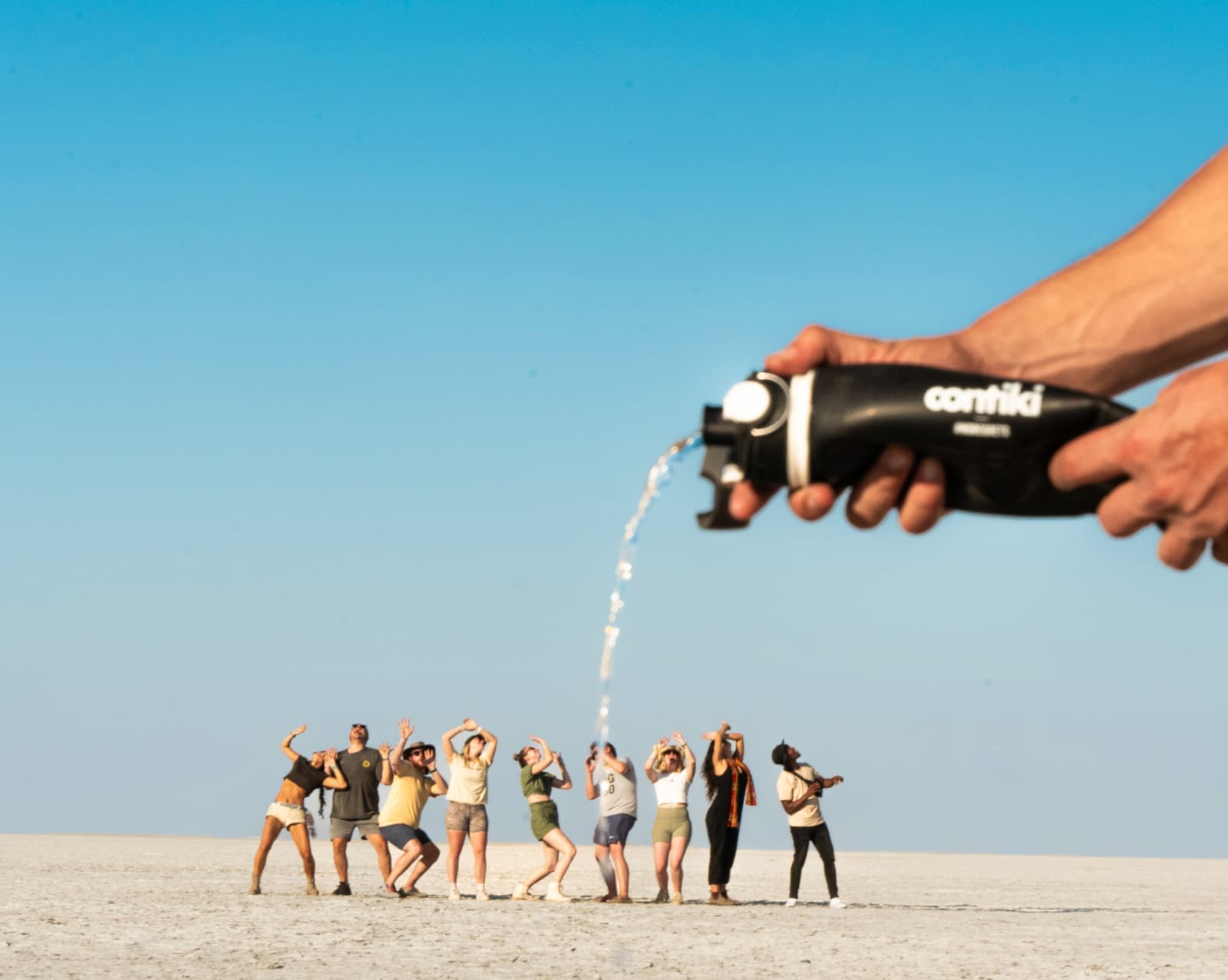Bottle of water in the foreground being thrown over travellers in the background at the Makgadikgadi Salt Pans, Botswana