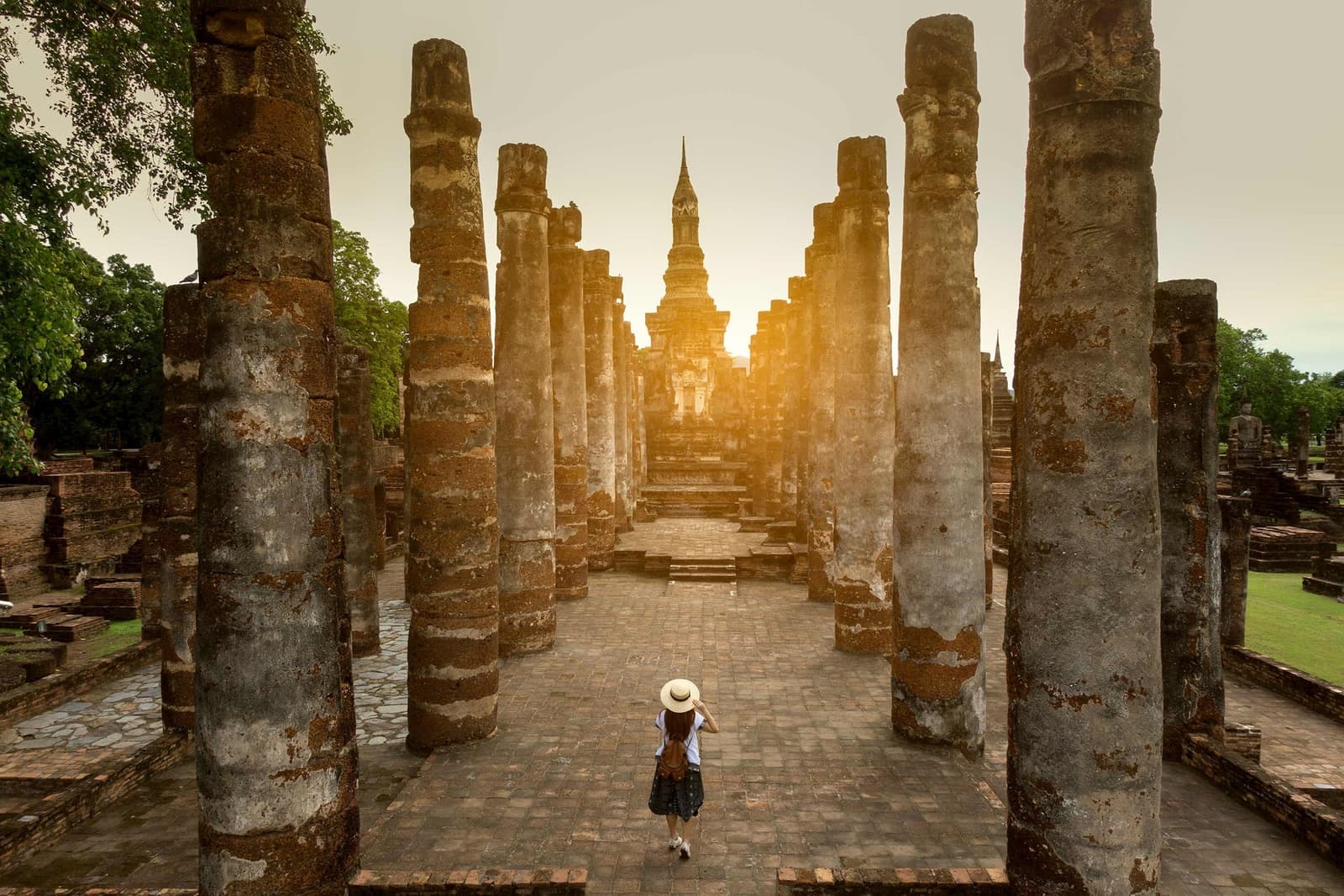Person walking along a pathway lined with stone columns at Sukhothai ruins, Thailand
