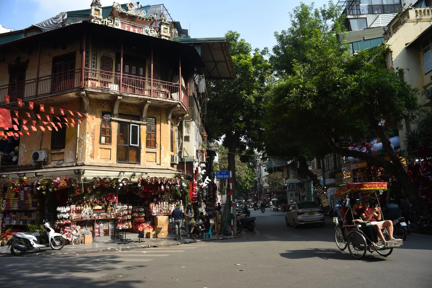 Lively street corner in Hanoi featuring traditional architecture and a passing rickshaw